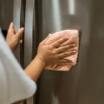 Woman cleaning a stainless steel refrigerator with a microfiber cloth