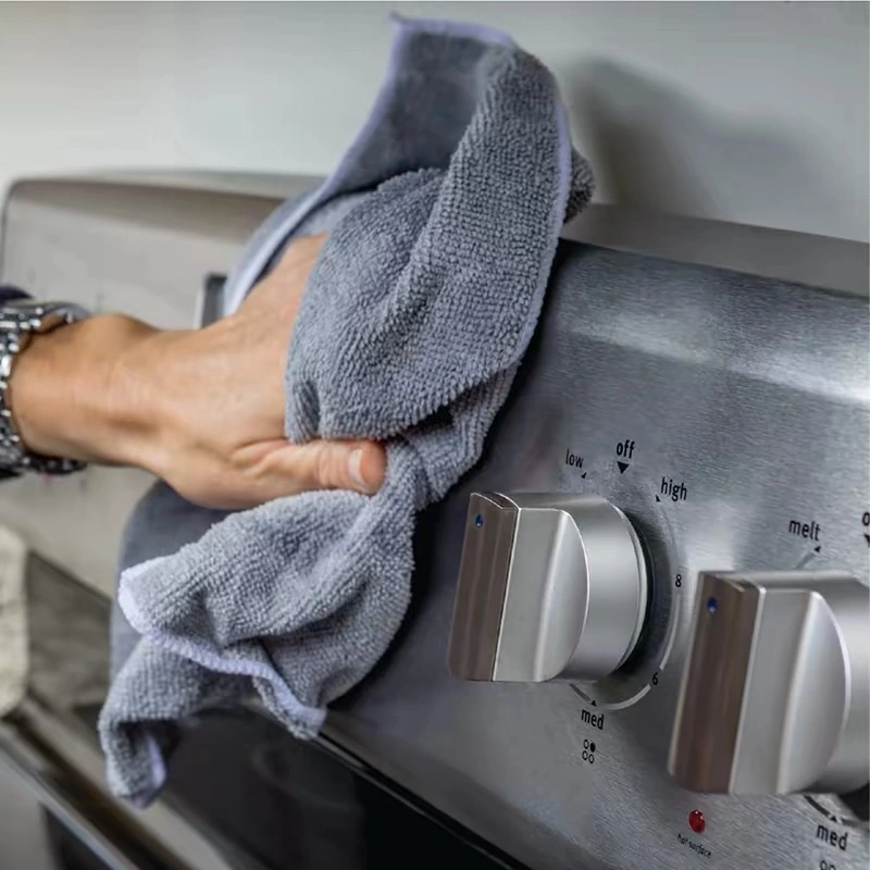 Hand wiping a stainless steel stove with a microfiber cloth to remove streaks and smudges