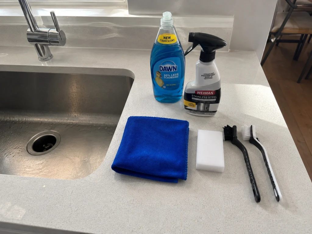 Stainless steel sink cleaning supplies arranged on a kitchen counter beside the sink