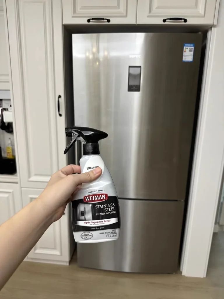 Weiman Stainless Steel Cleaner and Polish held in front of a stainless steel refrigerator