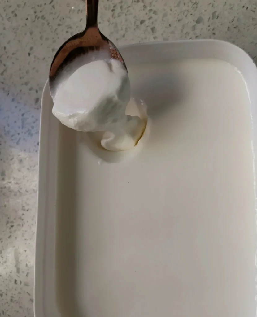A spoon lifting softly set homemade yogurt after fermentation