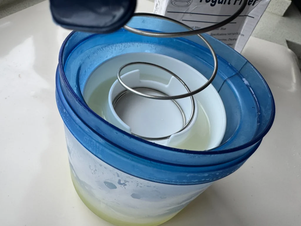 Open yogurt strainer showing the insert and collected whey after draining homemade yogurt