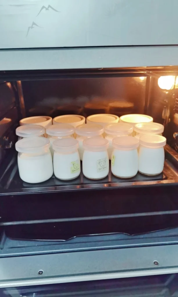 Jars of homemade yogurt incubating in an oven with the oven light on