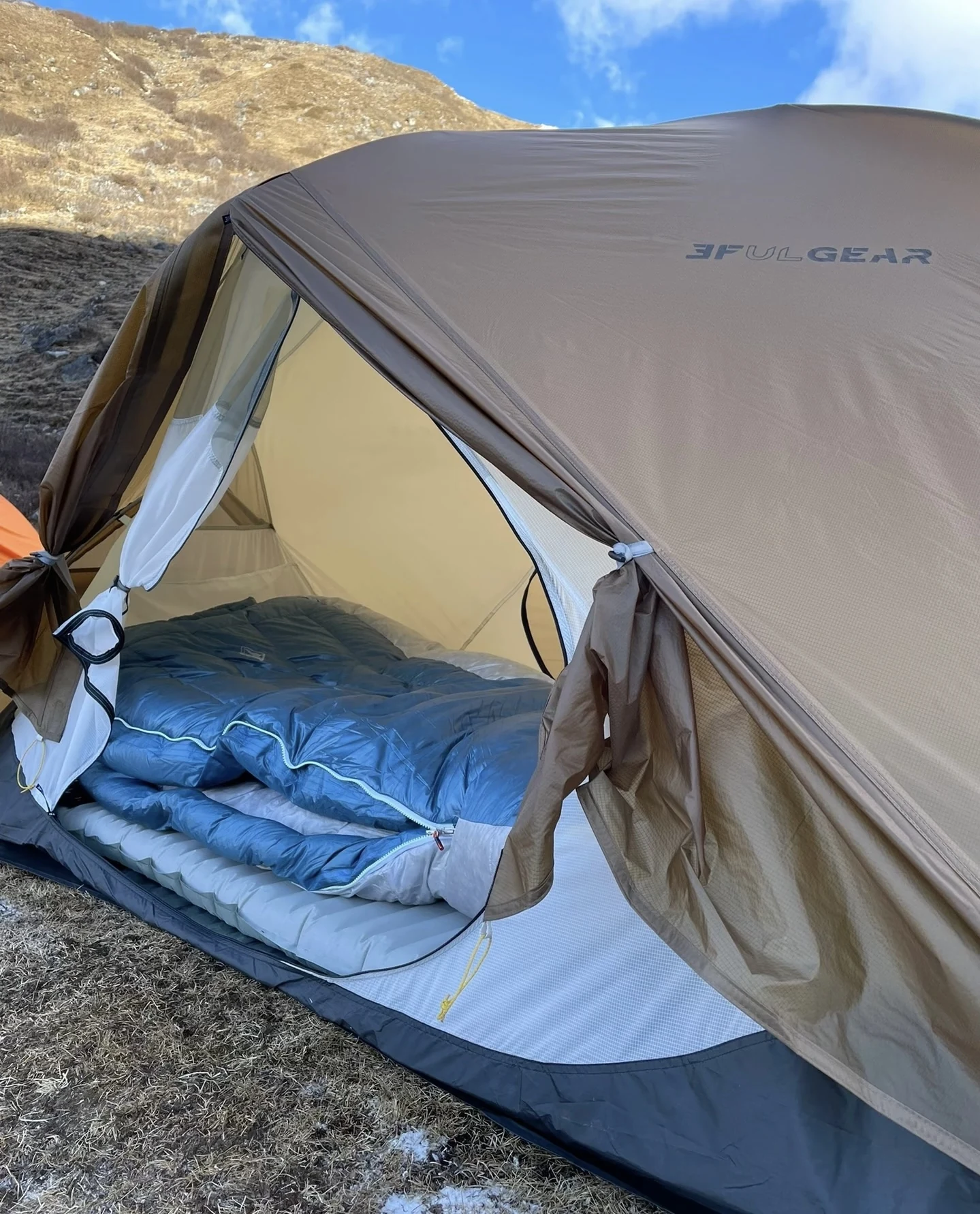 Blue sleeping bag resting on a light-gray inflatable sleeping pad inside an open tent.