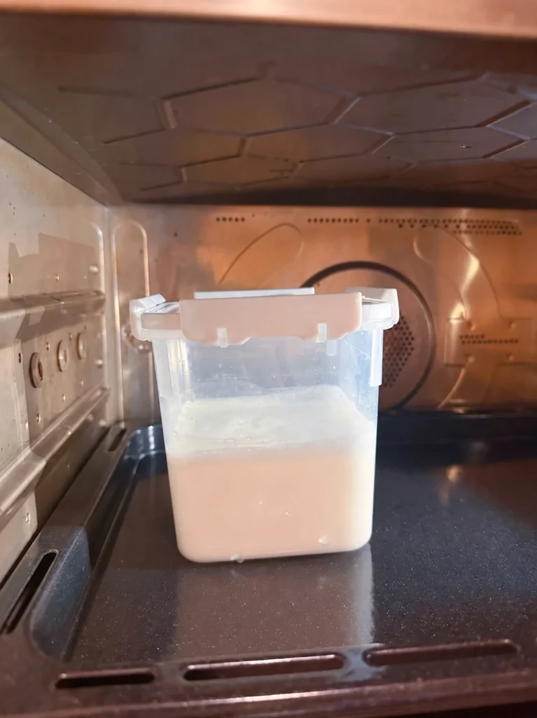 A covered translucent container of milk mixture on a tray inside an oven.