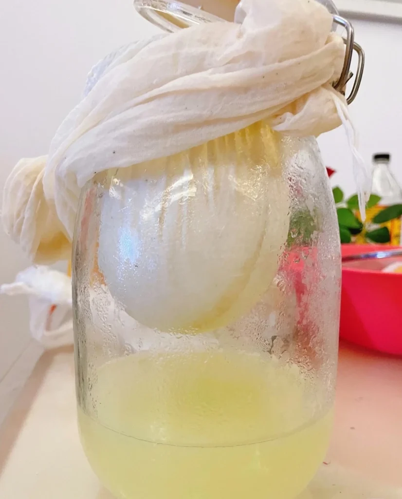 Yogurt held in a cloth above pale-yellow whey collecting in a clear glass jar.