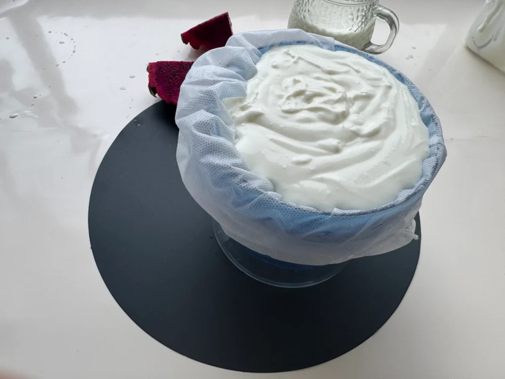 A blue cloth-lined strainer filled with yogurt on a dark round placemat.