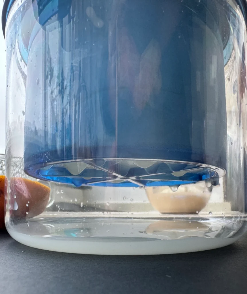 A close side view of a blue filter basket above a small amount of liquid in a clear container.