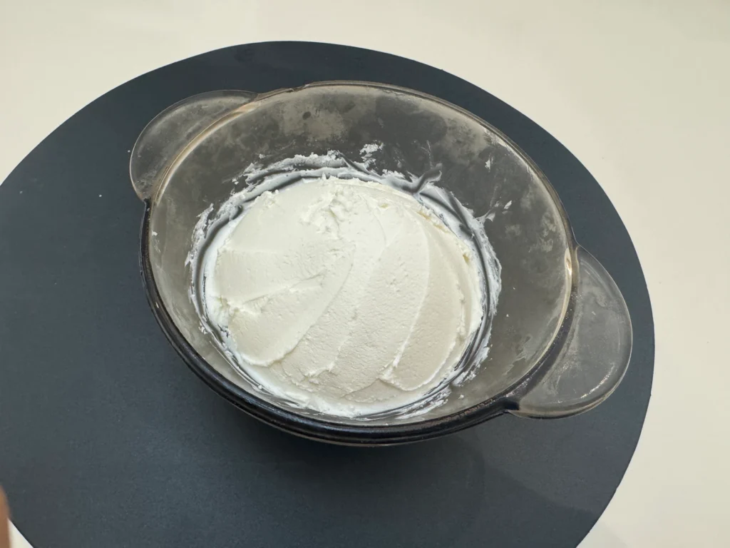 Plain thick strained yogurt in a handled glass bowl on a dark round placemat.