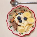 Yogurt bowl topped with banana slices, blueberries, almonds, and walnuts