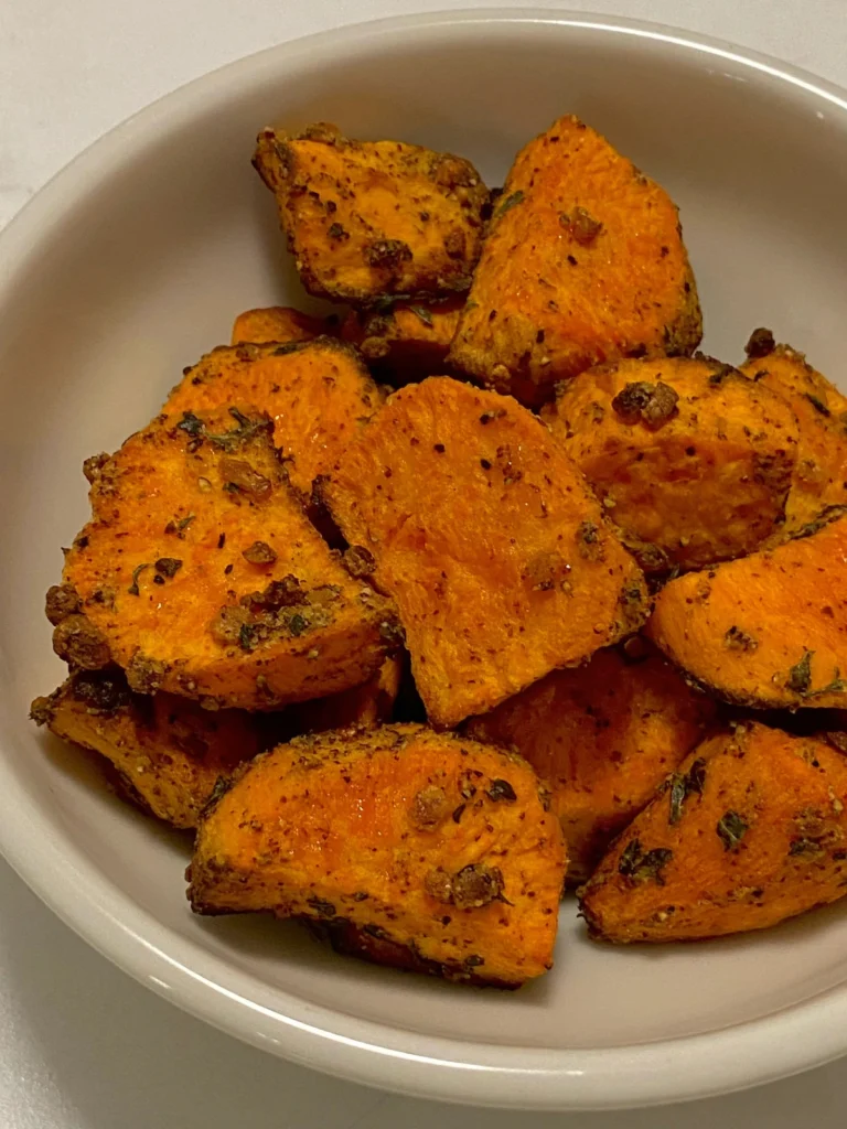 Air fryer sweet potato wedges seasoned with herbs and served in a white bowl.