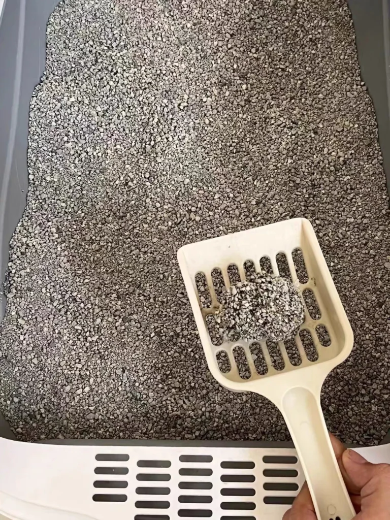 White litter scoop holding a clump of gray cat litter over a litter box