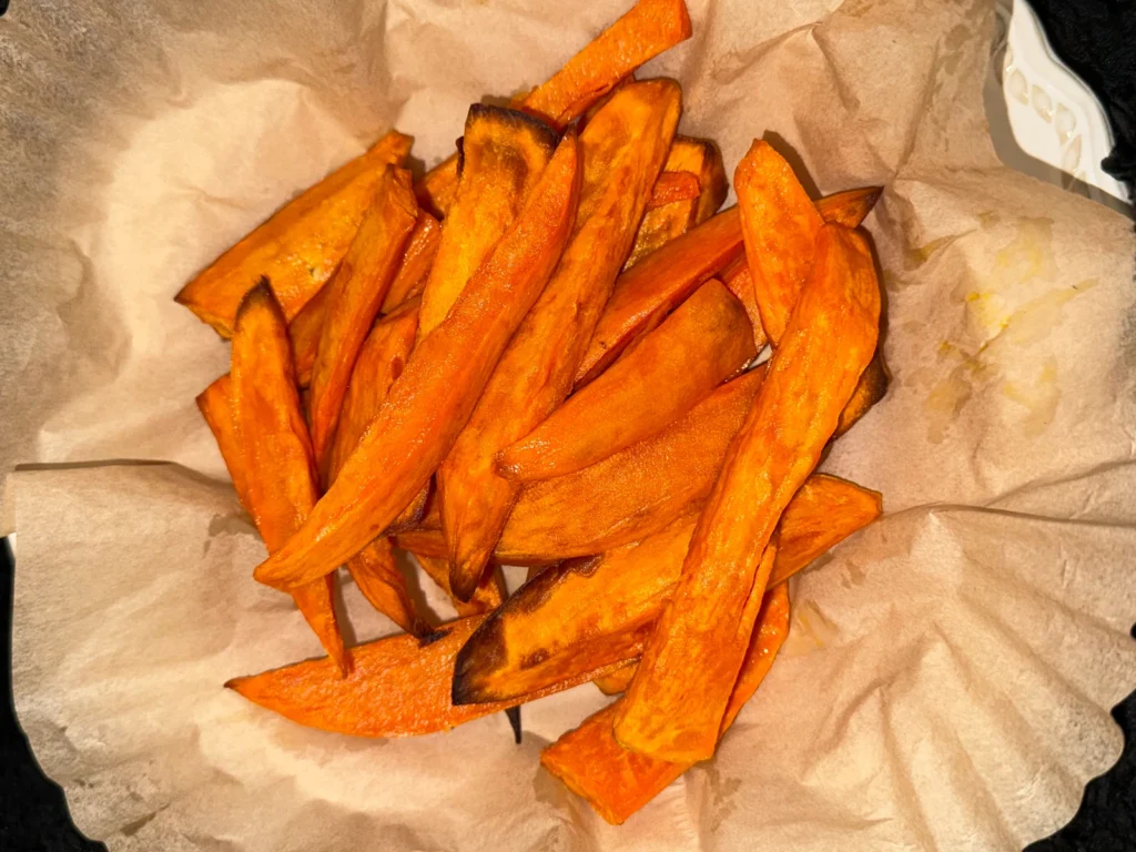 Air fryer sweet potato fries with browned edges on parchment paper.