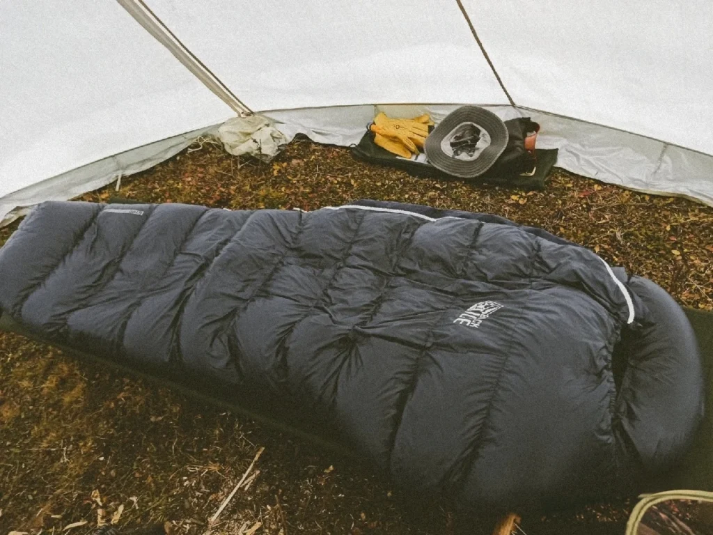 A dark sleeping bag laid out inside a camping tent with other gear near the back wall.