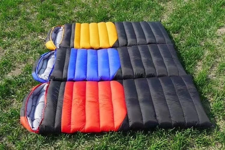 Three black sleeping bags with yellow, blue, and red panels laid out side by side on green grass.